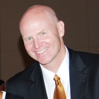 Charlie Daniel, Coverall CEO in a suit and tie smiling at the camera in a formal setting.