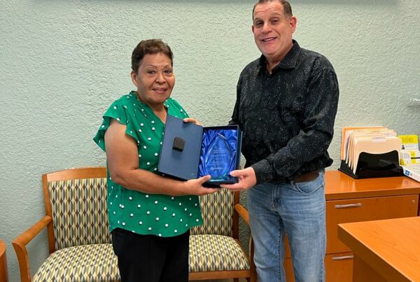 Two people holding an award, standing in an office with a "Coverall" sign behind them.