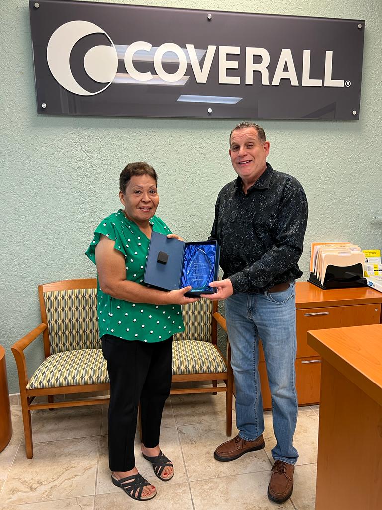 Two people holding an award, standing in an office with a "Coverall" sign behind them.