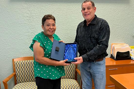 Two people in an office smiling and holding an award plaque.