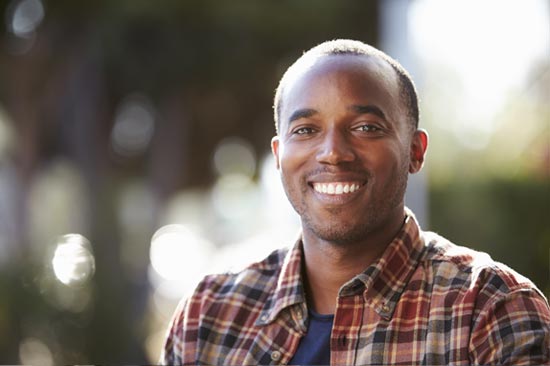 Smiling person outdoors in a plaid shirt, with blurred green background.