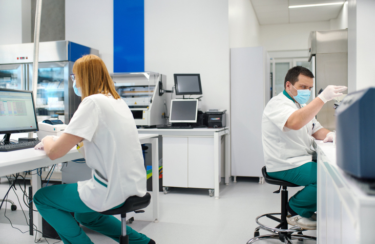 Scientists in masks conduct research in a lab, using computers and lab equipment, maintaining a sterile environment.