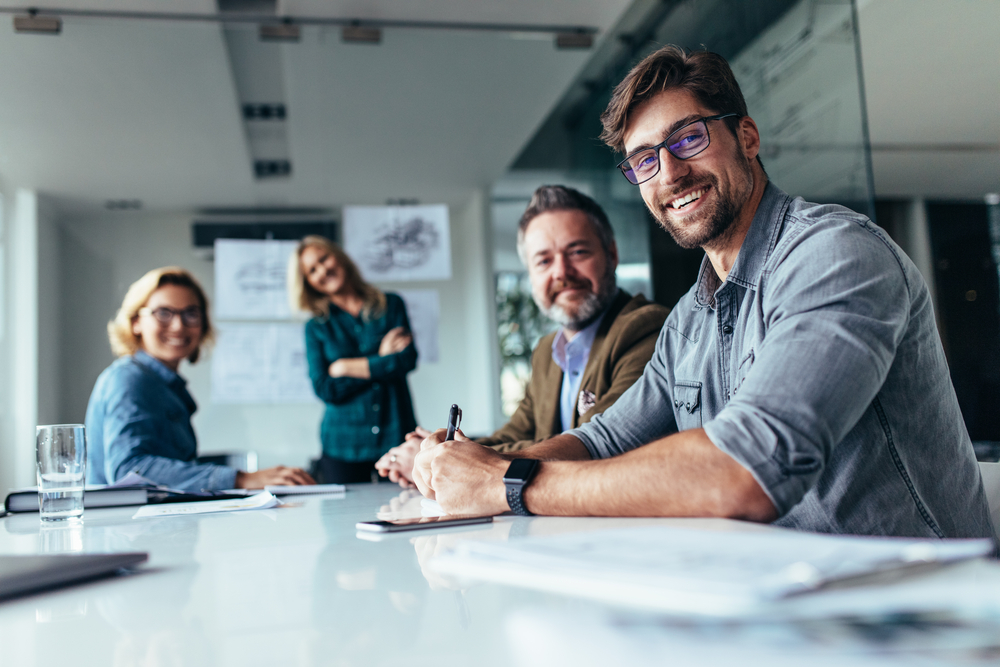 Team meeting in a modern office, with four people smiling and sitting around a table with documents.