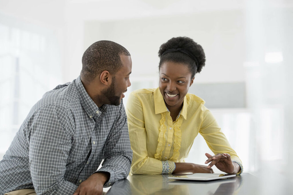 Two colleagues at a desk, engaging in a friendly conversation and smiling.