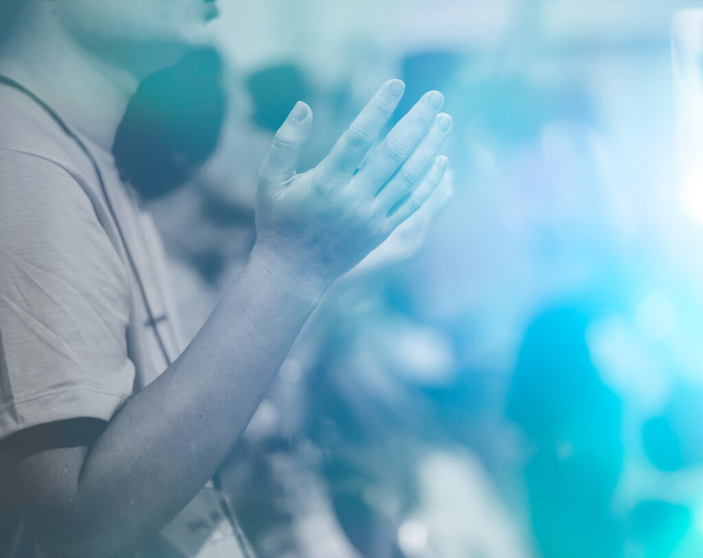 Person with raised hands in prayerful pose, surrounded by blue-tinted light.