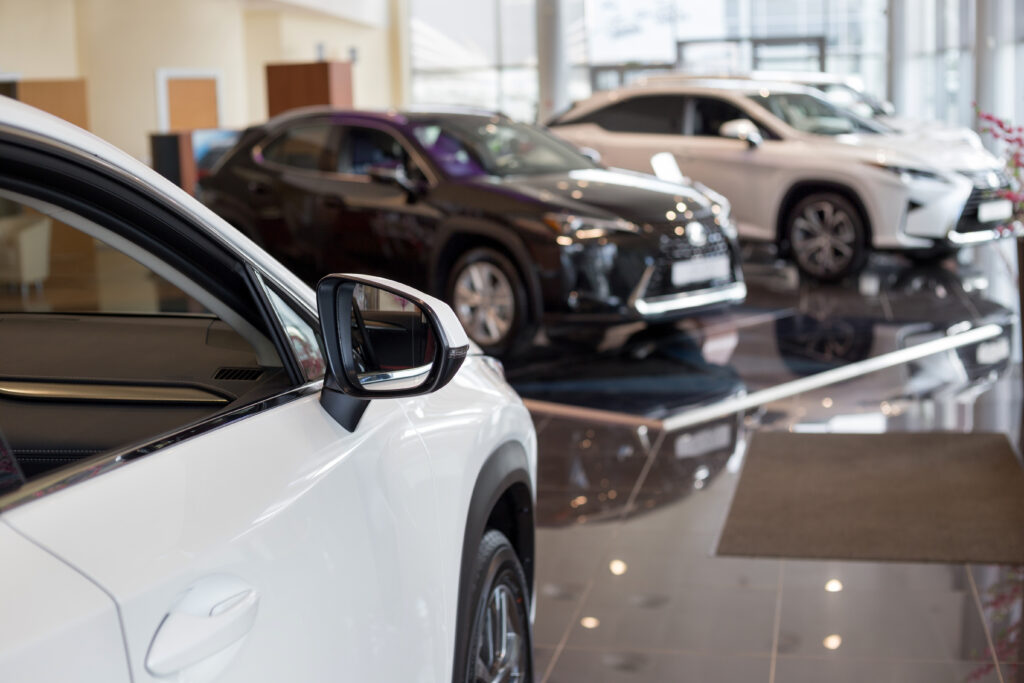 Cars displayed in a modern showroom with a focus on the side mirror of a white vehicle in the foreground.