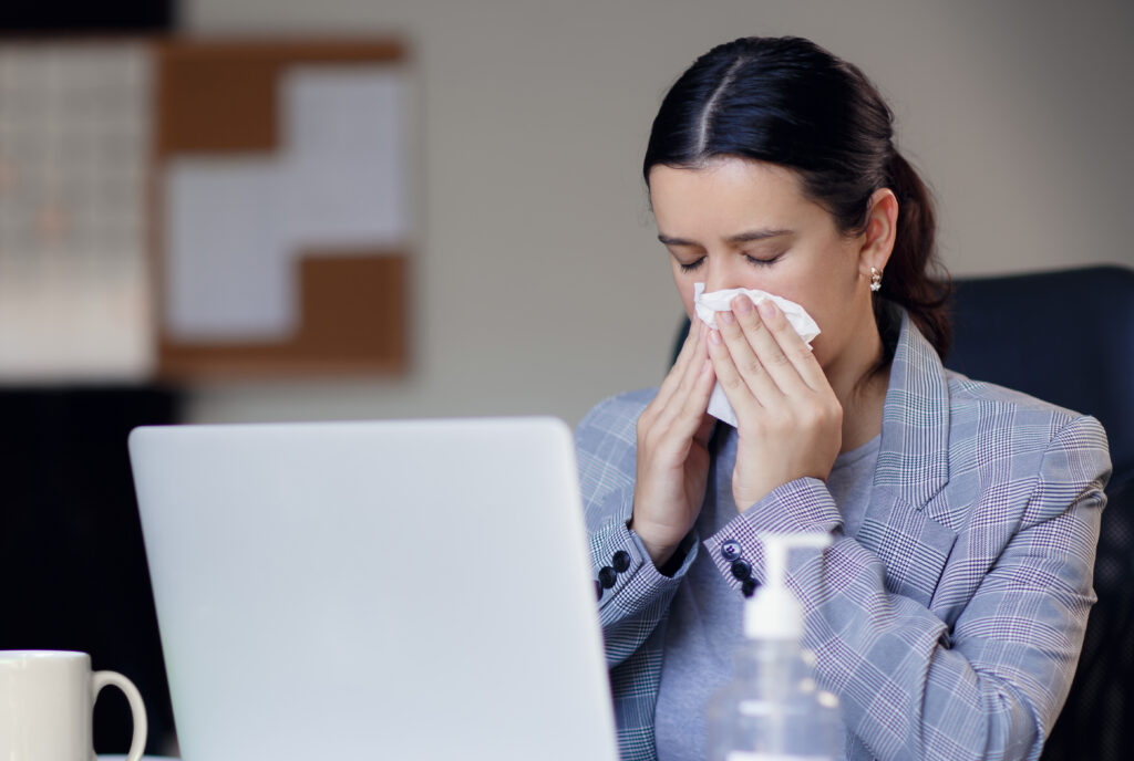 Person in office uses tissue, sitting at desk with laptop and sanitizer.