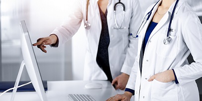 Two doctors in white coats review information on a computer screen.