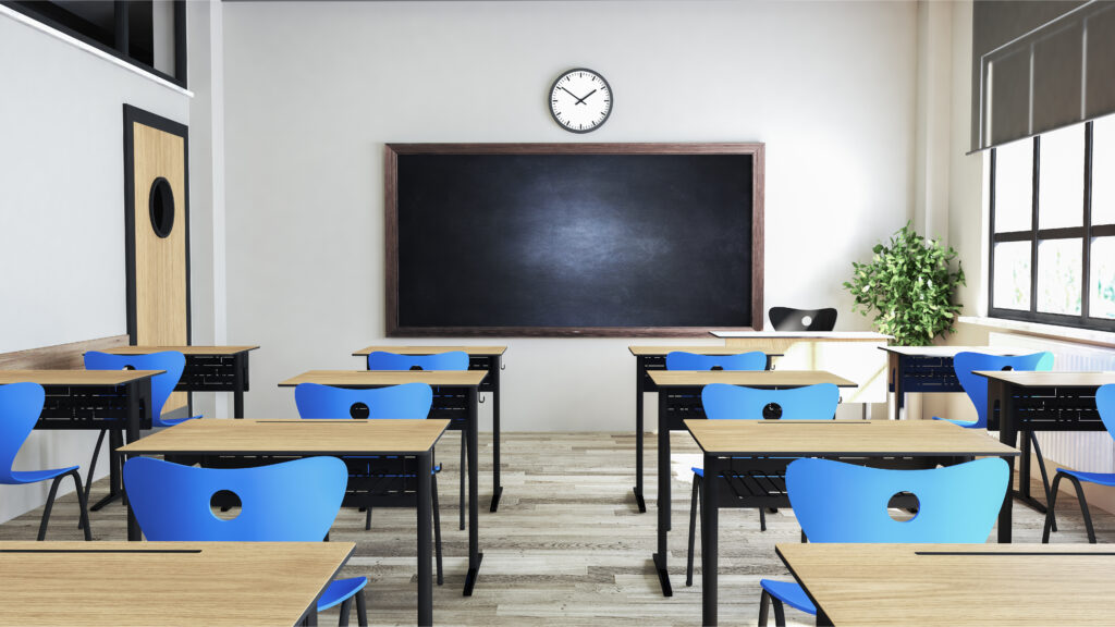 Empty classroom with blue chairs, wooden desks, a blackboard, wall clock, and a potted plant near the window.