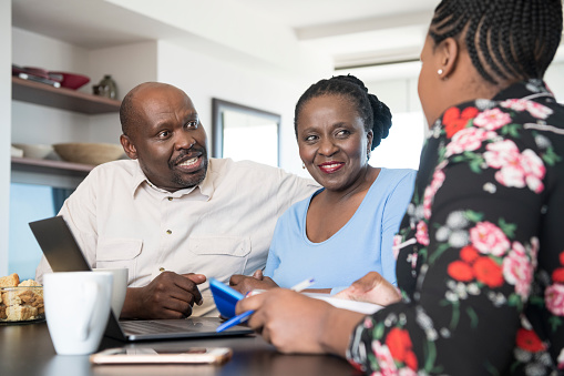 Three people having a discussion at a table with a laptop, notebook, and coffee mug.