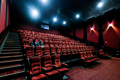 Empty movie theater with red seats, dim lighting, and a couple seated in the center of the auditorium.