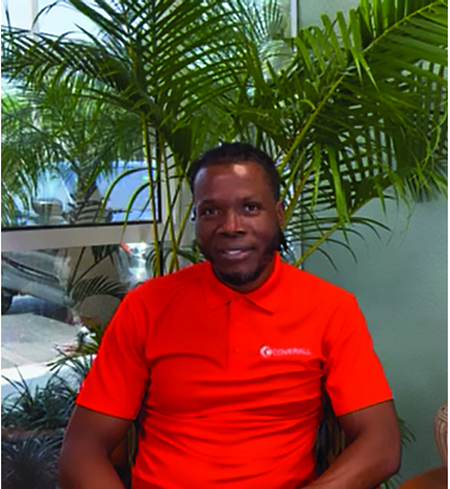 Man in a red polo shirt sits in a chair with green plants and large window in the background.