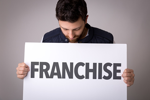 Man holding a sign that says "FRANCHISE" with a downward gaze.