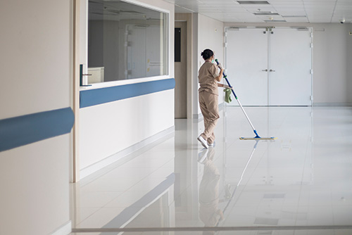 Person cleaning an empty hallway with a mop, wearing a beige uniform.