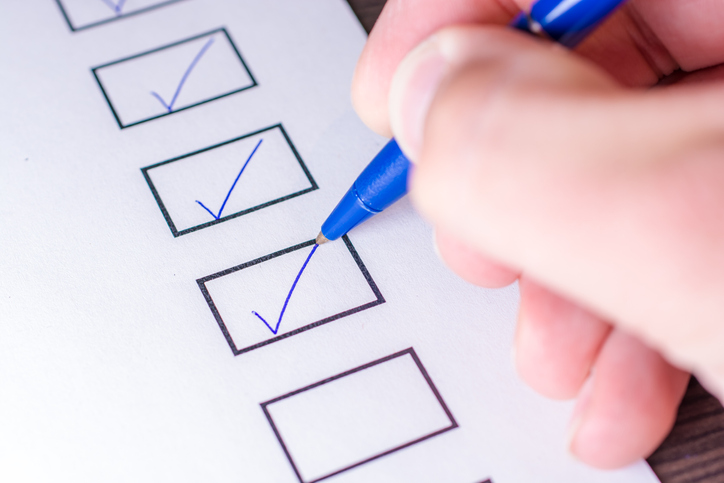Close-up of a hand checking boxes on a checklist with a blue pen.