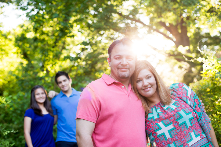 Four people pose together outdoors, with sunlight filtering through trees in the background.