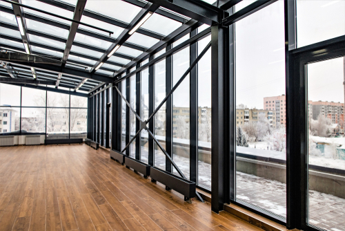 Spacious modern room with large windows, wooden floors, overlooking snow-covered cityscape. Natural light filling the space.