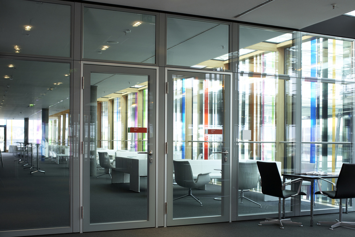 Modern office with glass walls, empty chairs, and tables, featuring colorful window reflections.