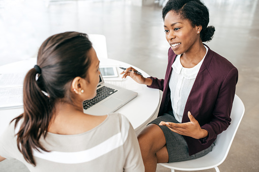 Two women sitting at a table, engaged in a work discussion with a laptop open in front of them.