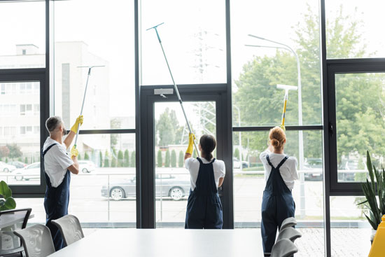 Workers cleaning large windows with squeegees in a modern office setting.