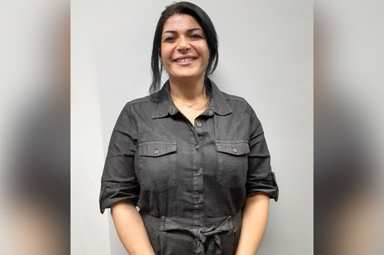 Smiling person in a gray button-up dress stands against a plain background.
