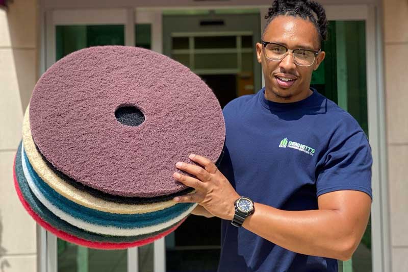 Man holding stacked floor buffer pads outside a building entrance.