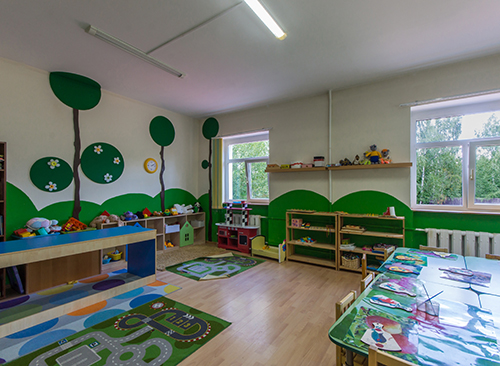 Colorful kindergarten classroom with toys, art supplies, and tree-themed wall decor.