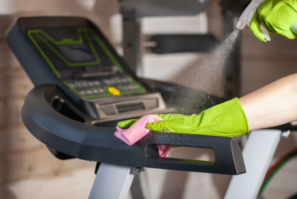 Person wearing gloves cleans treadmill with spray and cloth.