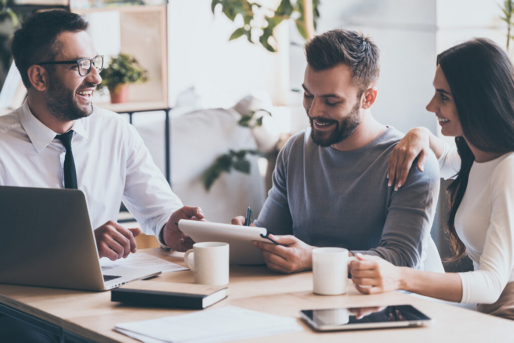 Three people having a positive meeting around a table with a laptop and tablets.