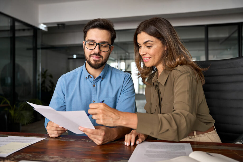 Two professionals reviewing documents together at a desk in an office setting.