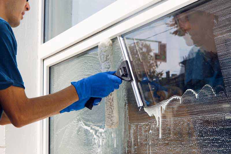 Person wearing blue gloves cleaning a window with a squeegee.