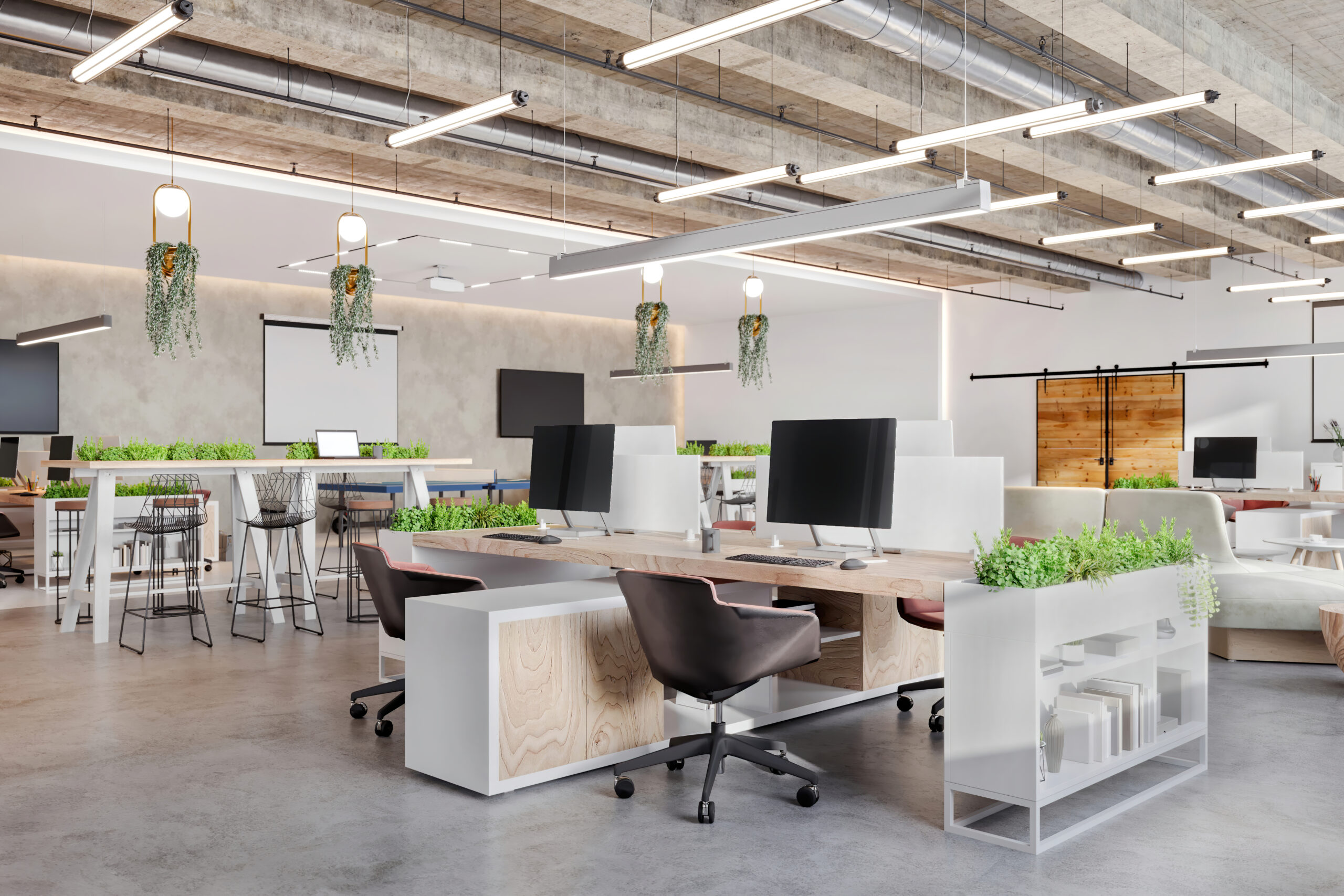 Modern office space with open layout, plants, desks, computers, and seating. Exposed ceiling with lights adds industrial styl