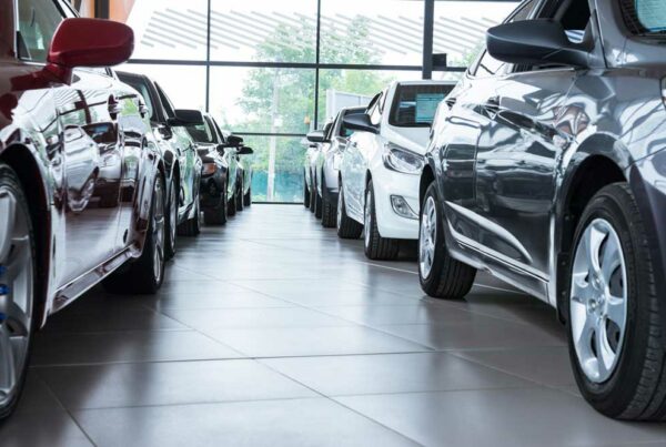 Cars are lined up inside a dealership showroom with a large window in the background.