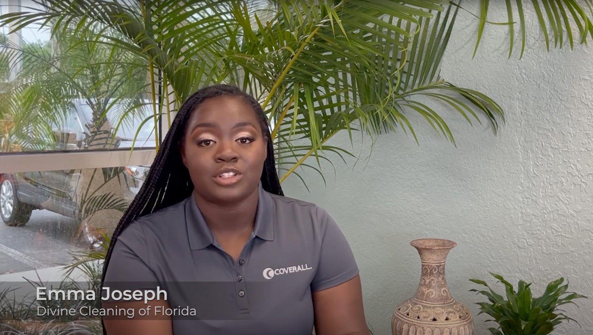 A person in a polo shirt sits indoors with plants and a decorative vase behind them, speaking directly to the camera.
