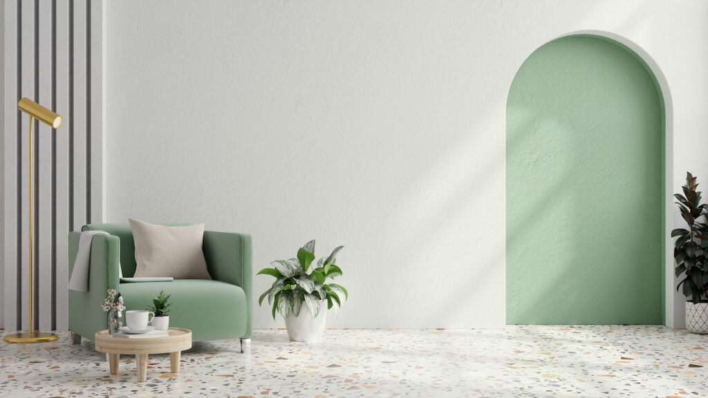 Minimalistic living room with a green couch, plants, a small round table, and arched green doorway. Terrazzo flooring.