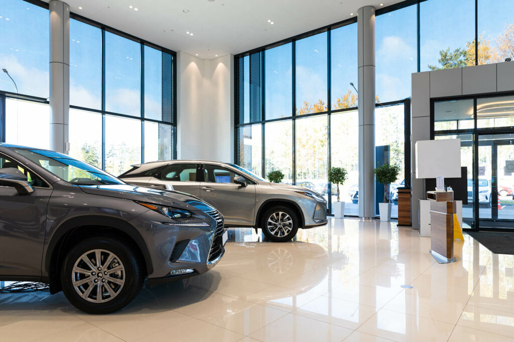 Car dealership showroom with two gray SUVs displayed on a glossy floor near large windows and modern decor.