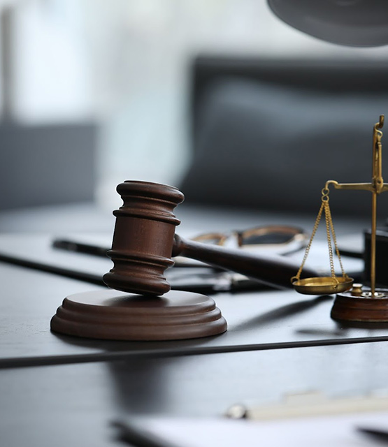 Wooden gavel and brass scales of justice on a desk, symbolizing law and legal proceedings.