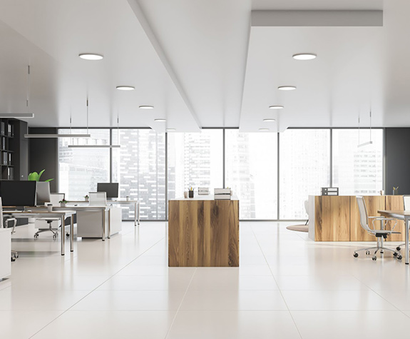 Modern office interior with large windows, wooden desks, and white tile flooring. Bright and spacious.