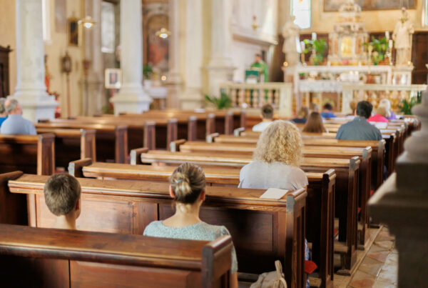 People seated in church pews facing a priest at the altar during service.
