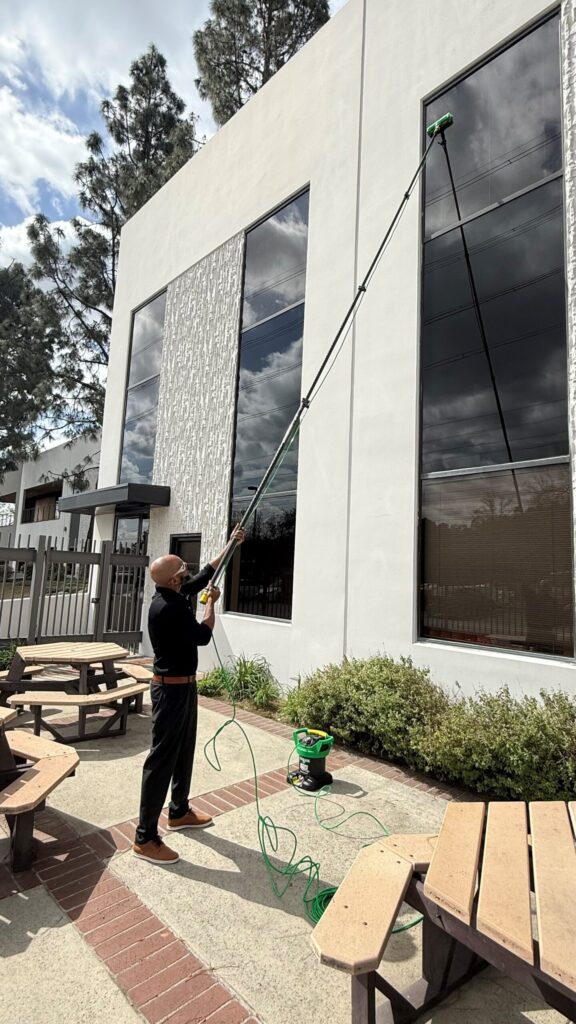 Male commercial cleaner cleaning the exterior office window using an extended pole.