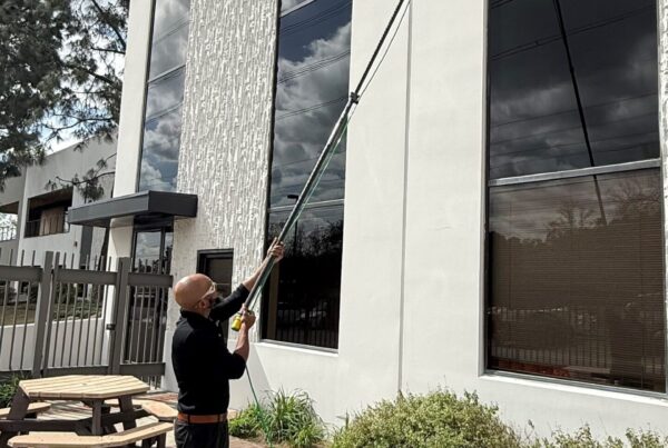 Male commercial cleaner cleaning the exterior office window using an extended pole.